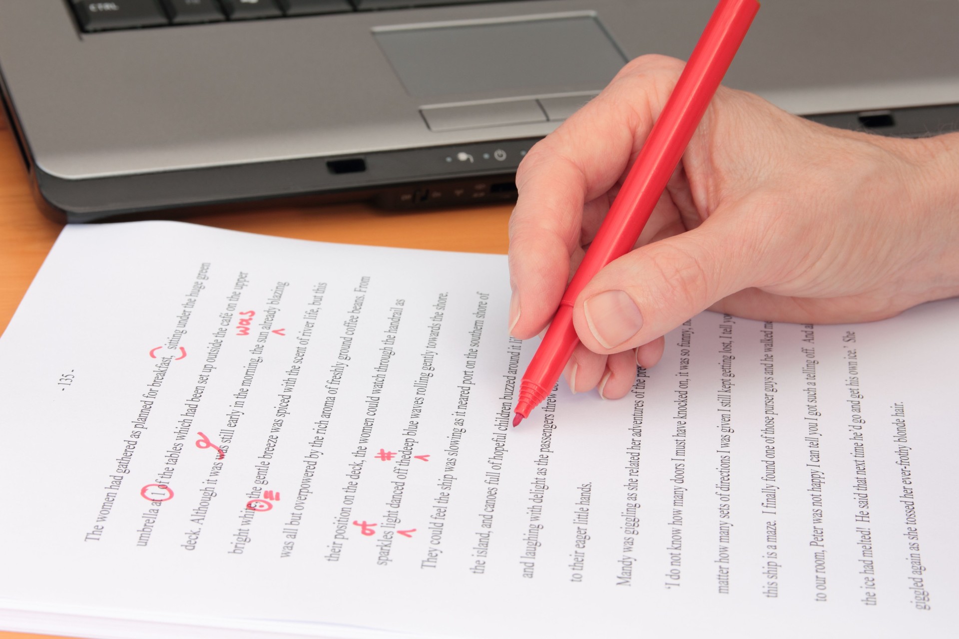 Hand Proofreading a Manuscript beside Laptop